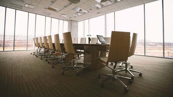 Empty boardroom showing long table and chairs with windows in background
